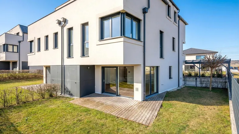 Moderne Hausfassade mit großem Garten und Holzterrasse.