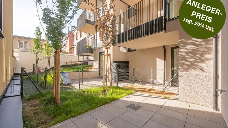 Eine gepflasterte Terrasse mit Grünflächen und jungen Bäumen vor einem modernen Neubau mit Balkonen.