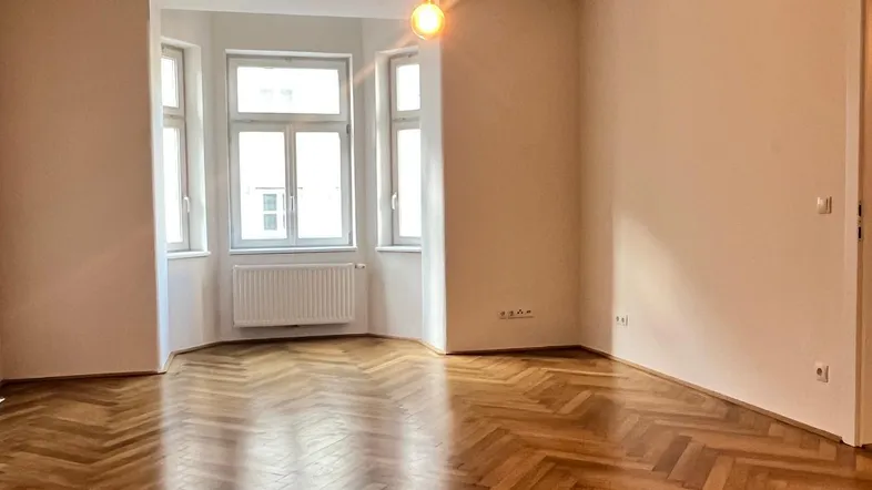 Helles Wohnzimmer mit klassischem Fischgrätparkett und Erkerfenstern, die viel Tageslicht hereinlassen.