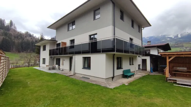 Modernes Mehrfamilienhaus mit Balkonen, gepflegtem Rasen und Bergblick in ländlicher Umgebung.