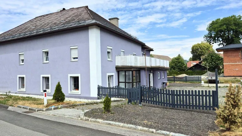 Ansicht des Hauses mit hellvioletter Fassade, weißen Fensterrahmen und kleinem Balkon.