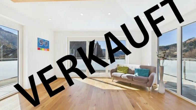 Helles Wohnzimmer mit Holzboden, großen Fenstern, Bergblick und sichtbarem Deckenbalken.