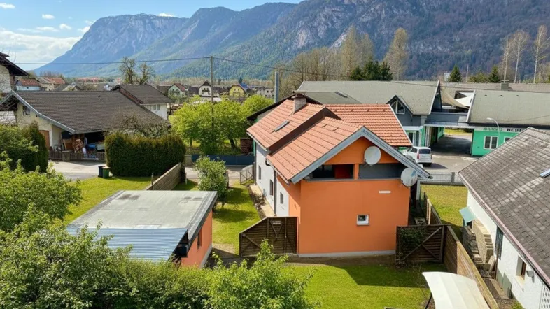 Blick auf das Haus mit Garten und umliegender Berglandschaft unter blauem Himmel.