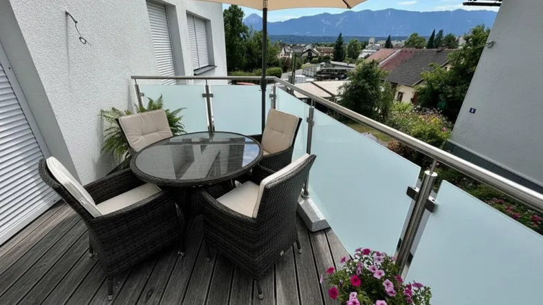 Möblierter Balkon mit Holzboden, Glasgeländer und weitem Blick auf die Berge und die Umgebung.