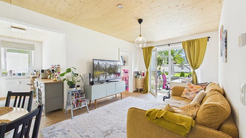 Offener Wohn-Essbereich mit gelbem Sofa, Holzbalkendecke und Zugang zur Terrasse.