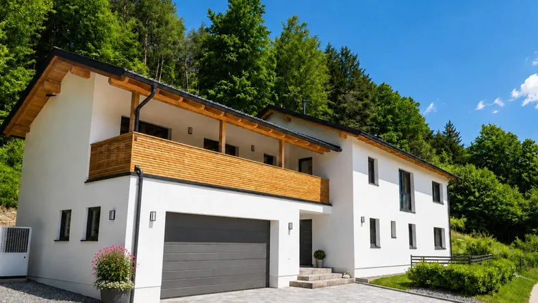 Modernes Einfamilienhaus mit weißer Fassade, Doppelgarage und Holzdetails am Balkon.