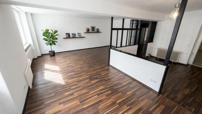 Helles Wohnzimmer mit dunklem Holzboden und moderner Raumaufteilung, die vielseitige Nutzung ermöglicht.