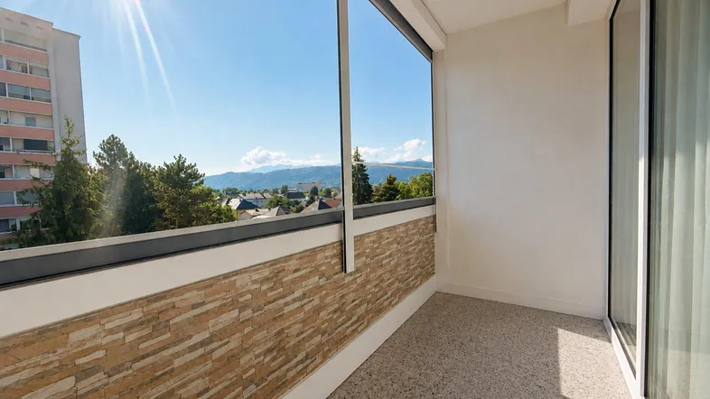 Heller Balkon mit Steinverkleidung und weitem Blick über die Stadt und die Berge.