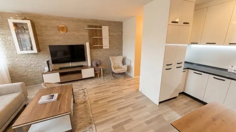 Moderner offener Wohnbereich mit heller Holzoptikboden und integrierter Küche, ideal für geselliges Beisammensein.