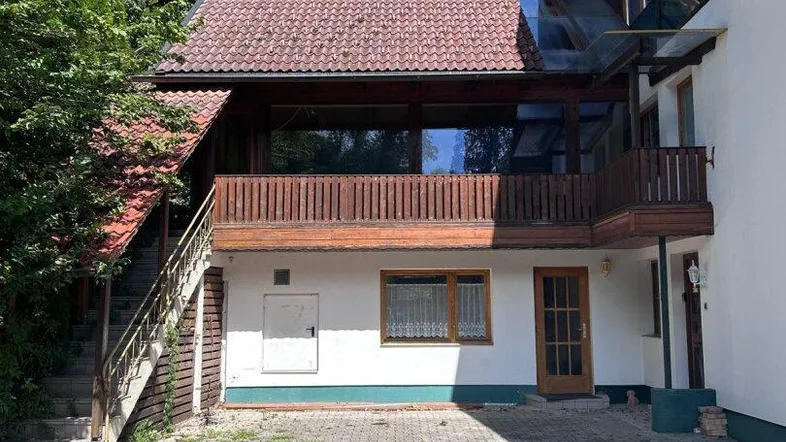 Ansicht des Hauses von vorne mit Balkon, Außentreppe und gepflastertem Vorplatz.