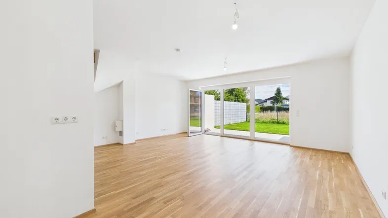 Helles Wohnzimmer mit Holzboden und großen Fenstern, die Zugang zum Garten bieten.