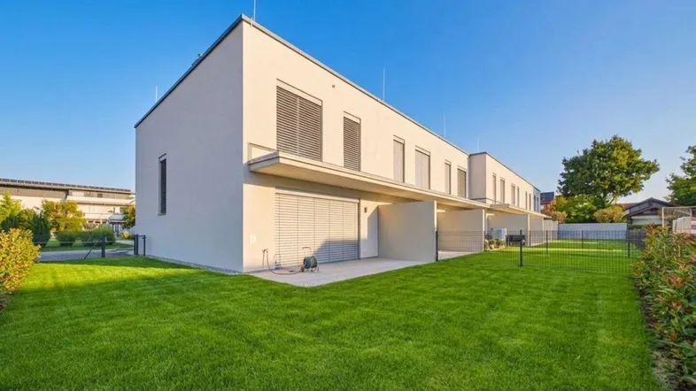 Moderne Reihenhäuser mit gepflegtem Rasen und privatem Gartenbereich unter blauem Himmel.