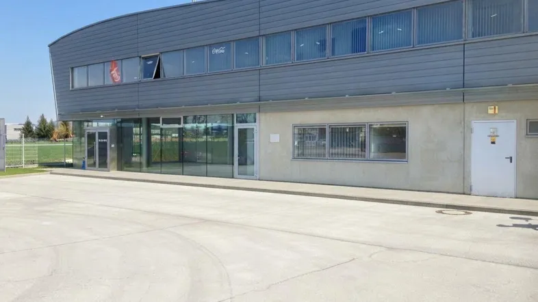 Modernes Geschäftsgebäude mit geschwungener Fassade, großen Fenstern und einem geräumigen Parkplatz davor.