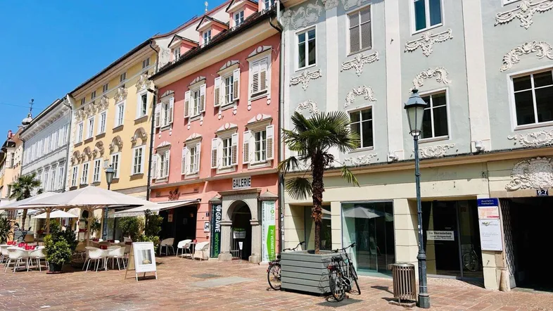 Blick auf eine belebte Straße mit historischen Gebäuden, Geschäften und Außengastronomie unter blauem Himmel.