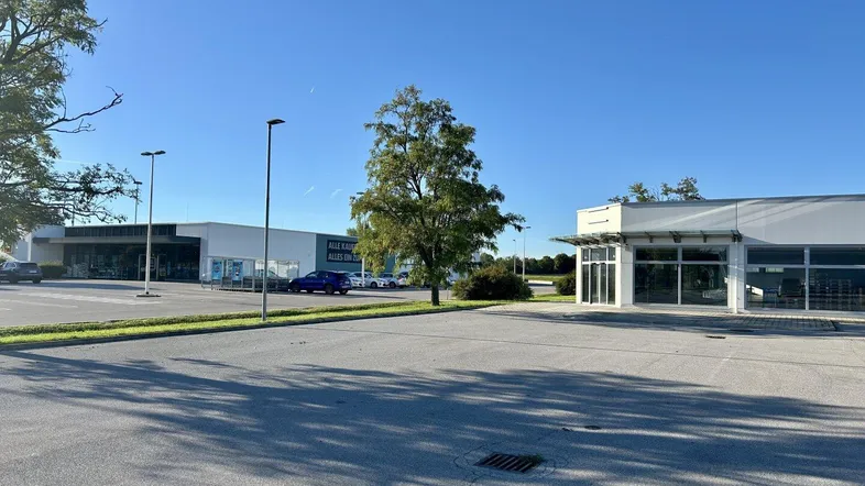 Weitläufiger Parkplatz vor einem modernen Geschäftsgebäude unter blauem Himmel mit Bäumen im Hintergrund.