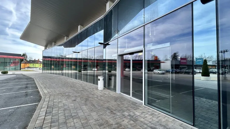 Moderne Geschäftsfassade mit großer Glasfront und Eingangsbereich, umgeben von einem Parkplatz.