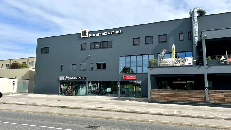 Modernes Geschäftsgebäude mit großen Glasflächen und einem Fitnessstudio-Schild unter blauem Himmel.