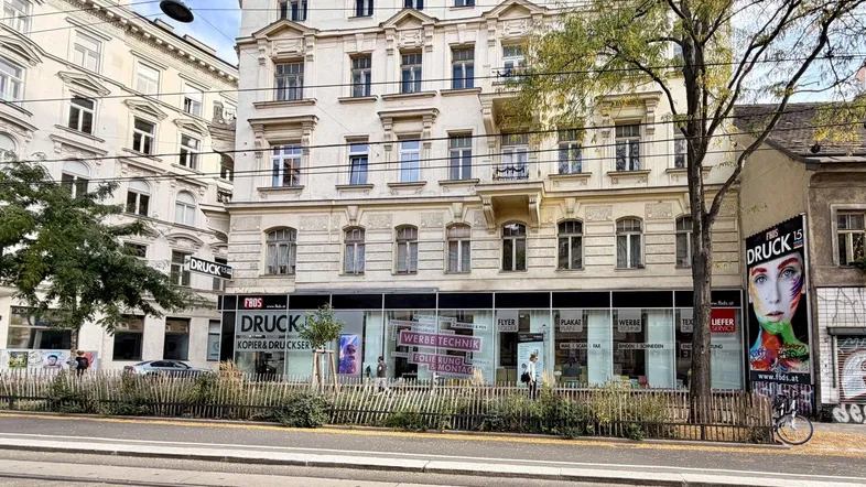 Klassisches Gebäude mit Geschäftsflächen im Erdgeschoss und Wohnungen darüber, an einer belebten Straße gelegen.
