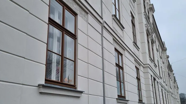 Ansicht der weißen Fassade eines Altbaus mit braunen Fenstern und klassischer Architektur.