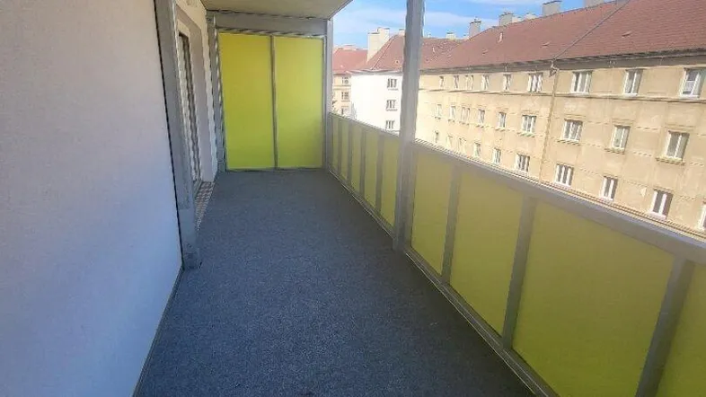 Heller Balkon mit gelb-grünen Sichtschutzelementen und Blick auf die umliegenden Gebäude.