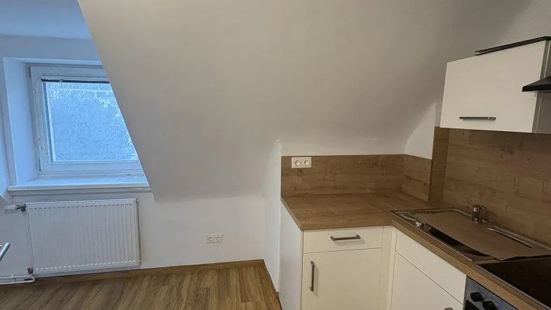 Kleine Küche im Dachgeschoss mit Schrägdecke, Laminatboden und Fenster.