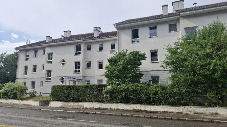 Mehrfamilienhaus mit heller Fassade und grüner Hecke entlang der Straße.