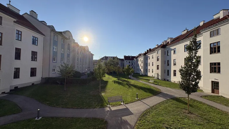 Sonniger Innenhof mit Grünflächen, Wegen und Bänken, umgeben von Wohngebäuden.