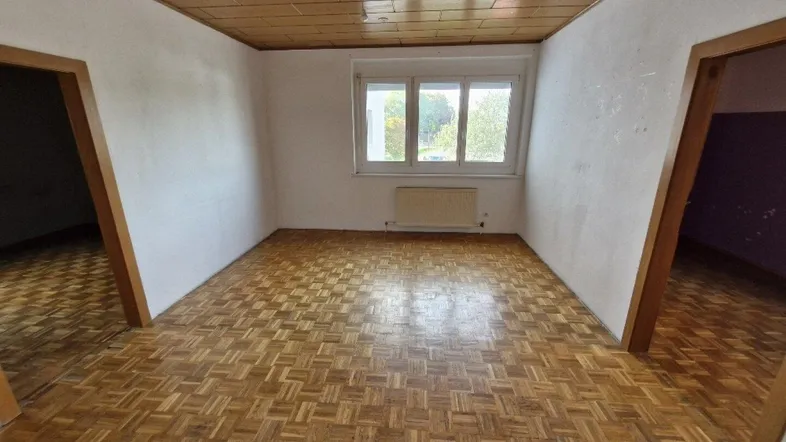 Geräumiges Zimmer mit Holzdeckenverkleidung und Parkettboden, bereit für Renovierung und individuelle Gestaltung.