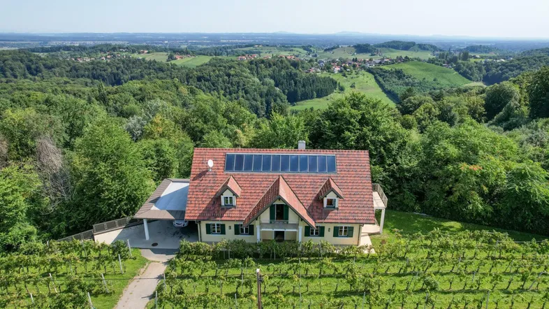 Luftaufnahme eines Hauses mit Solaranlage, umgeben von Weinbergen und grüner Hügellandschaft.