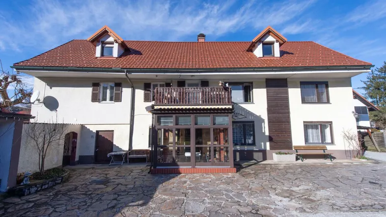 Die Vorderansicht des Hauses mit rotem Ziegeldach, Wintergarten und gepflasterter Einfahrt.