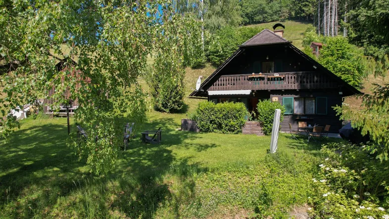 Traditionelles Holzhaus mit Satteldach und großem Garten in grüner Hanglage, umgeben von Bäumen.