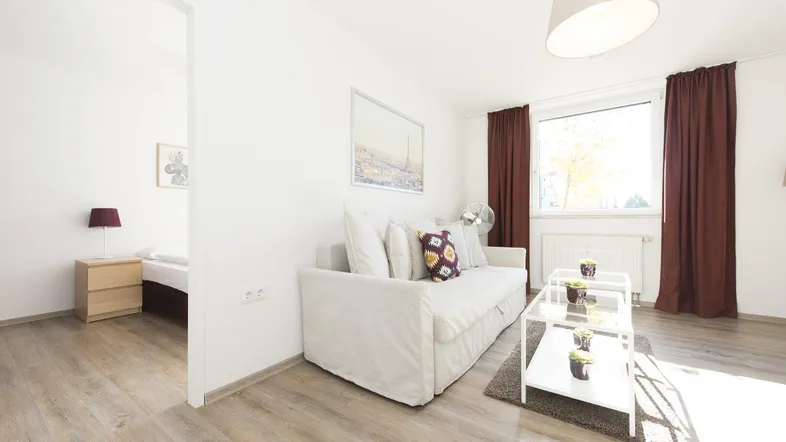 Helles Wohnzimmer mit modernem Sofa, Holzboden und Blick in ein angrenzendes Schlafzimmer.