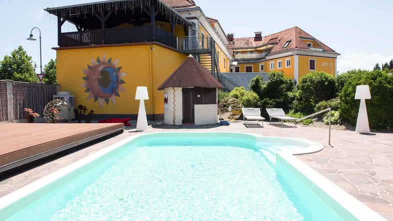 Außenbereich mit großem Pool, Liegestühlen und einem charmanten gelben Gebäude im Hintergrund.