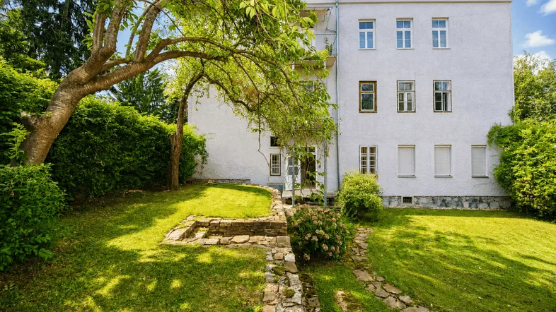 Gepflegter Gartenbereich mit altem Baum und grüner Rasenfläche vor dem Wohngebäude.