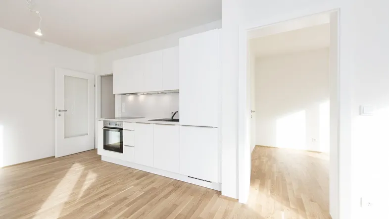 Helles, offenes Wohnzimmer mit integrierter weißer Küche und hellem Parkettboden.