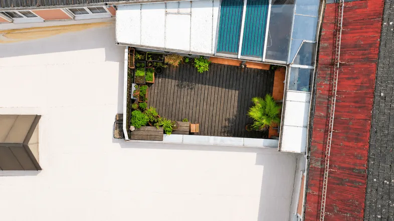 Dachterrasse mit Holzboden, Pflanzen und Glasüberdachung, von oben betrachtet, bietet einen privaten Außenbereich.