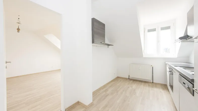 Helle Küche mit Dachschrägen, Laminatboden und Blick in einen weiteren Raum.