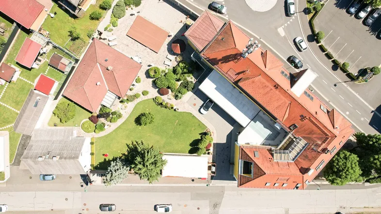 Luftaufnahme eines Gebäudekomplexes mit umliegenden Häusern, Straßen und Parkplätzen.