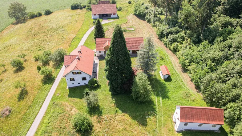 Luftaufnahme eines Anwesens mit mehreren Gebäuden, umgeben von grünen Feldern und Wäldern.