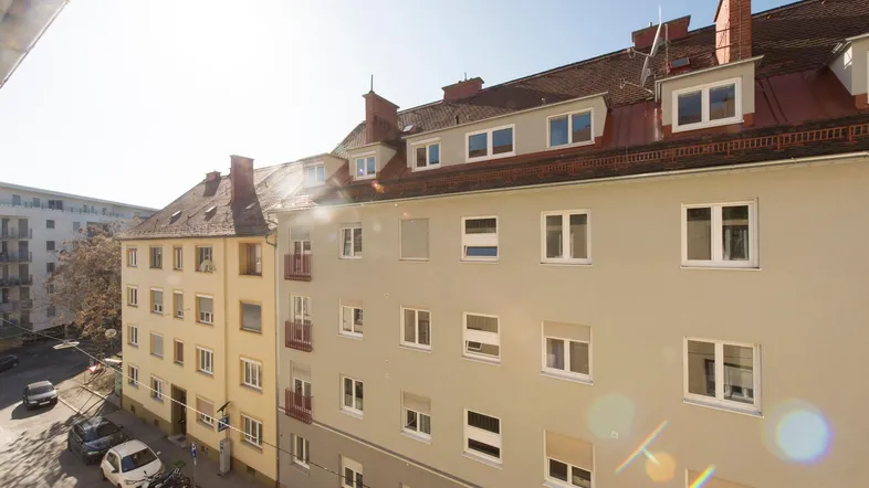Gebäudefassade mit mehreren Fenstern und Dachgauben, darunter eine belebte Straße mit parkenden Autos.