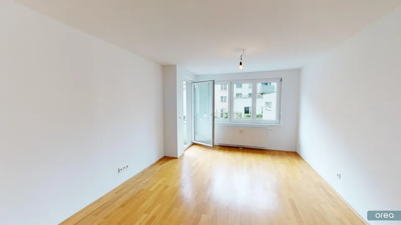 Helles Wohnzimmer mit Parkettboden und Zugang zu einem kleinen Balkon, bietet Blick auf umliegende Gebäude.