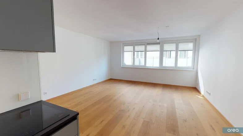 Heller Wohnbereich mit Parkettboden und großen Fenstern, angrenzend an eine moderne Küche.