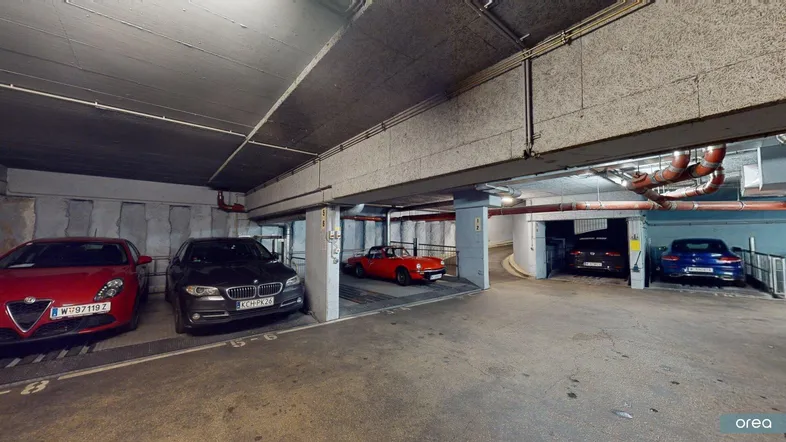 Geräumige Tiefgarage mit mehreren Stellplätzen, Betonwänden und sichtbaren Installationen.