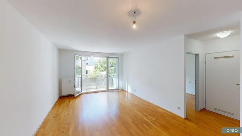 Helles Wohnzimmer mit Parkettboden, weißen Wänden und Zugang zu einem Balkon.
