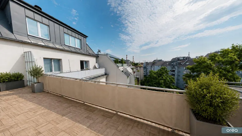 Geräumige Dachterrasse mit Holzbodenfliesen, Pflanzen und Blick über die Stadt.