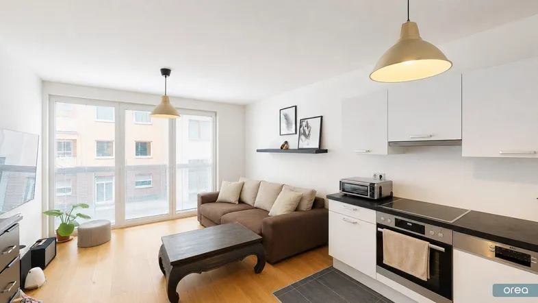 Heller offener Wohnbereich mit integrierter Küche, Holzboden und Zugang zum Balkon.