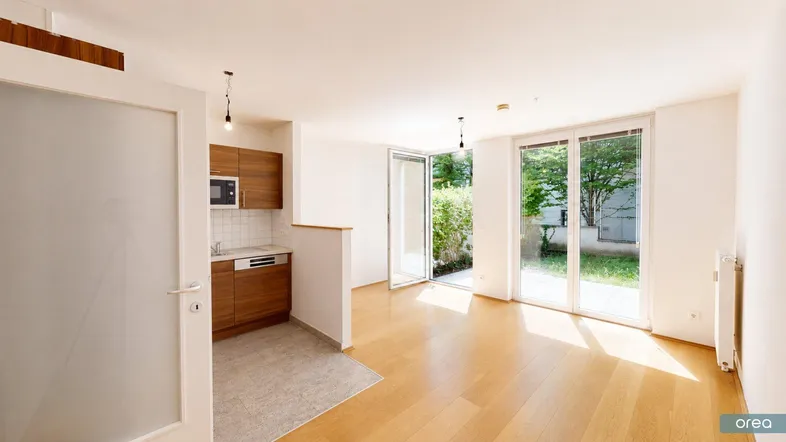 Helles Wohnzimmer mit integrierter Küchenzeile, Parkettboden und Zugang zum Garten.