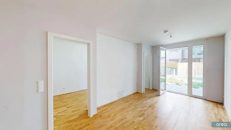 Helles Zimmer mit Holzboden und Zugang zu einer kleinen Terrasse oder Gartenbereich.