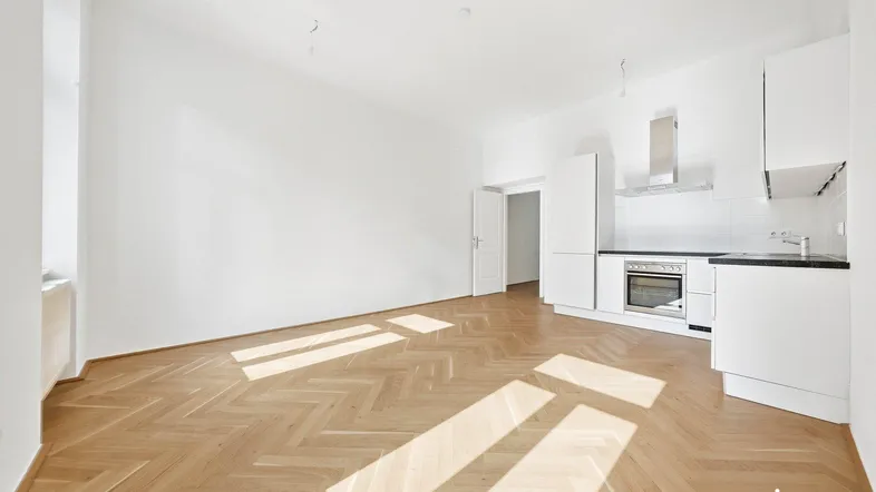 Helles Zimmer mit Fischgrätparkettboden und integrierter Küchenzeile, ideal für offenes Wohnen.