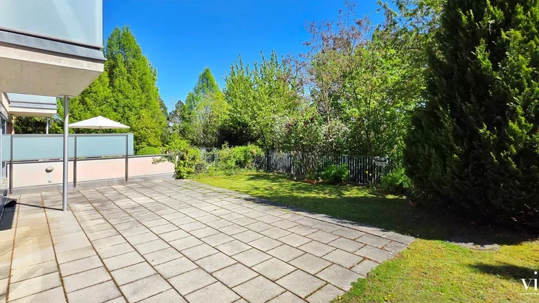 Geräumige gepflasterte Terrasse mit angrenzendem Rasen und üppiger Bepflanzung.